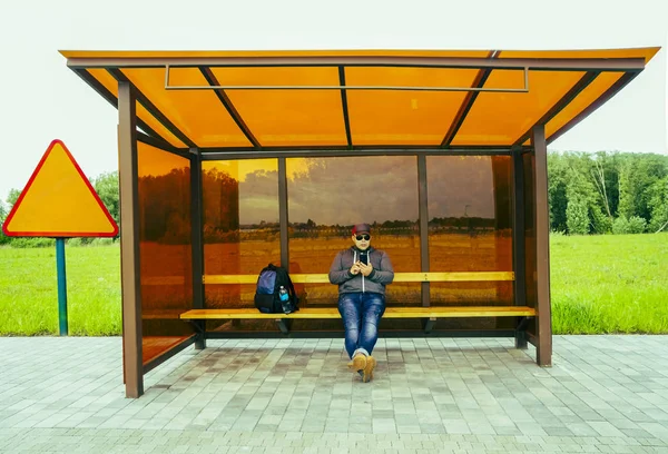 Jovem Alegre Está Esperando Por Transporte Parada Ônibus Masculino Sentado — Fotografia de Stock