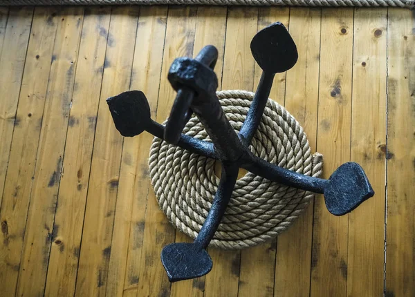 black metal anchor and rope on wooden floor.