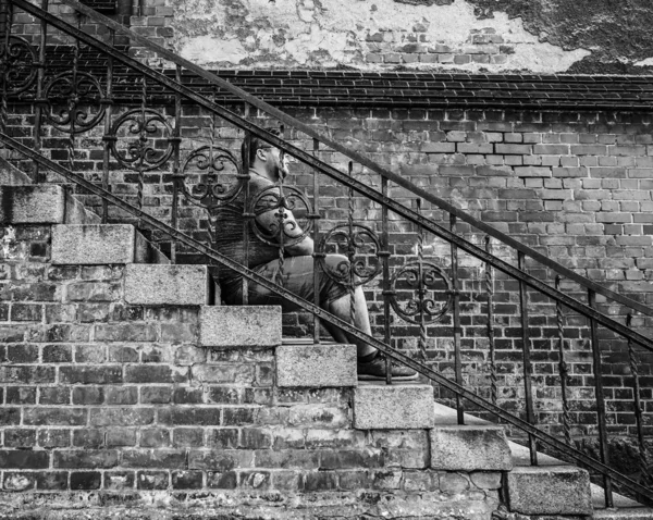 handsome pensive man sitting on steps on  bricked building background. portrait of young brunet guy in depression sitting near  brick wall.