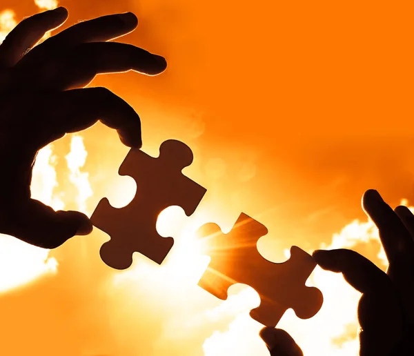 two hands trying to connect couple puzzle piece with sunset back