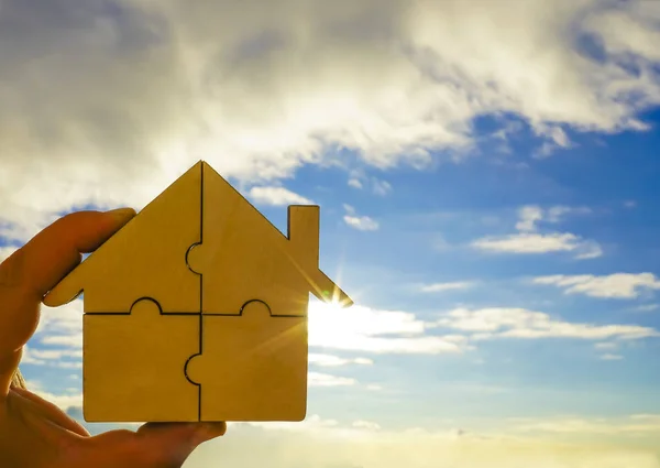 hand holding   wooden house puzzle on blue  sky background.