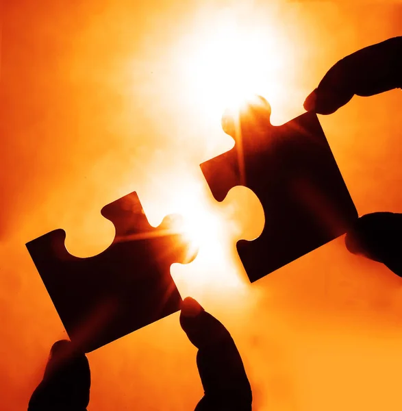 Duas mãos tentando conectar a peça de quebra-cabeça casal com o pôr do sol de volta — Fotografia de Stock