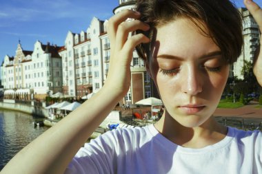 Portre büyüleyici kısa saçlı esmer kız beyaz bir t-shirt, gözleri kapalı, parlak bir Güneşli günde bir nehir tarafından beton bir iskelede güneş ışığı zevk