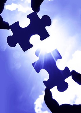 Gökyüzü arka planında yapboz parçaları olan eller.  