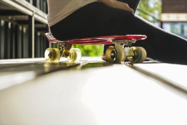 güzel gün batımı sırasında set üzerinde oturan tozluk ve t-shirt giymiş bir patenci kız yan görünümü.