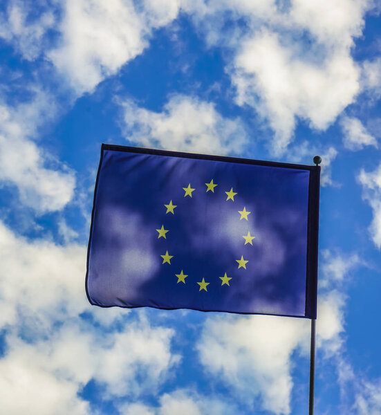 Flag of the European Union waving in the wind on flagpole against blue sky on sunny day, close-up