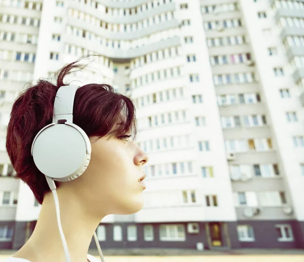 A girl  listening to music from her handheld mp3 or mobile phone. Happy young woman  listening to music and dancing in the street. Low angle view