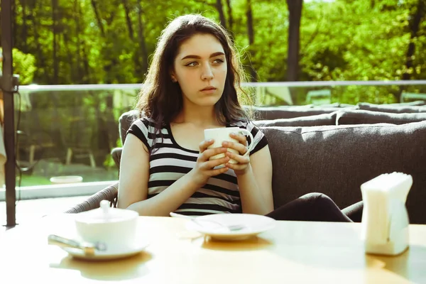 Kız kafenin balkonunda kahve fincan zevk. Sokak kafede kahve içen ciddi genç bayan Portresi.