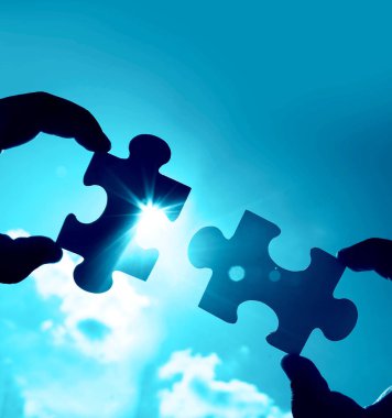 Gökyüzü arka planında yapboz parçaları olan eller.  