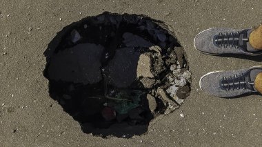 Yolda büyük derin saksı deliği. kuru kötü bakım. Trafik için tehlikeli. Araçlarda hasar