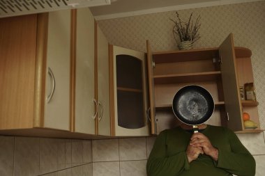 Yüzünü tavayla kaplayan genç bir adam. Ev mutfağında çekilen fotoğraf.