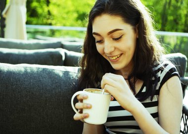 Kız kafenin balkonunda kahve fincan zevk. Sokak kafede kahve içen mutlu genç bayan Portresi. 