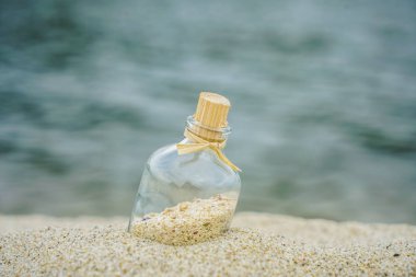 Beyaz kuma gömülmüş deniz kabukları olan şişe.yaz plajı ve arka planda mavi su. 