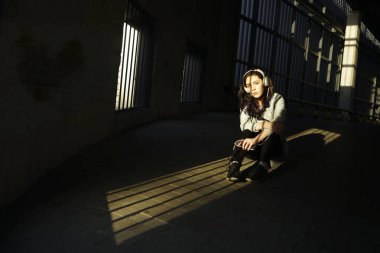 Neşeyle dinleniyor. Güzel genç kadın müzik dinliyor ve otoparkta yerde oturuyor.güneşli ışık ve gölgeler yüzünde