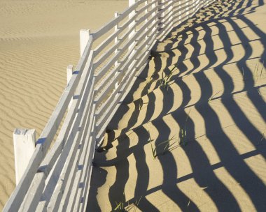 geç öğleden sonra güneşsahil boyunca beyaz ahşap çıta çit düşük açı görünümü. Bir kıyı bariyer adada parlak bir kumul boyunca kum çit ve gölgeler desen parçası. Güneşli öğleden sonra yüksek açı görünümü