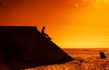 Kırmızı tuğla duvar üstünde oturan adam Yan görünümü - merdiven, güneş gökyüzü bulutları arka plan ile. erkek siluet. 