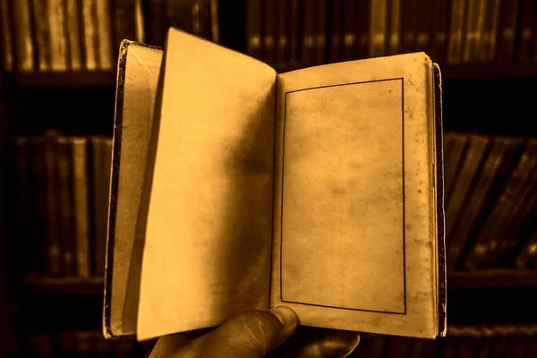 図書館で本を読んでいる男子学生 ぼかし本棚の背景を持つ古いヴィンテージブックを保持する手 空のコピースペース 空白ページ — ストック写真