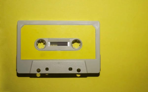 黄色の紙のテーブルの上にレトロな灰色のカセットテープ トップビュー コピースペース — ストック写真