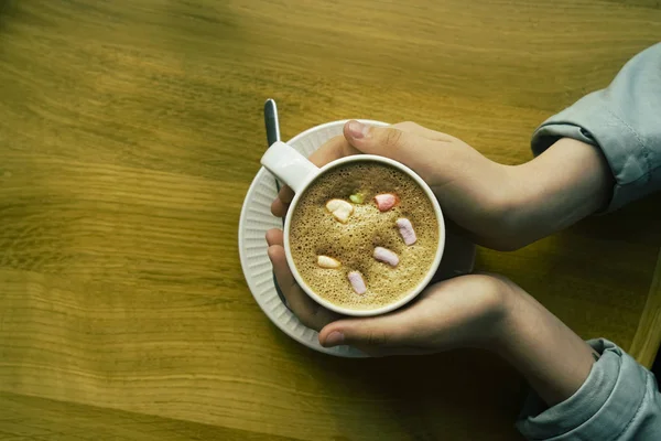 cup of cocoa with marshmallows in hands. Winter hot drink. girl warm hands from the mug with hot cocoa or chocolate with sweets on wooden table from above. top view.