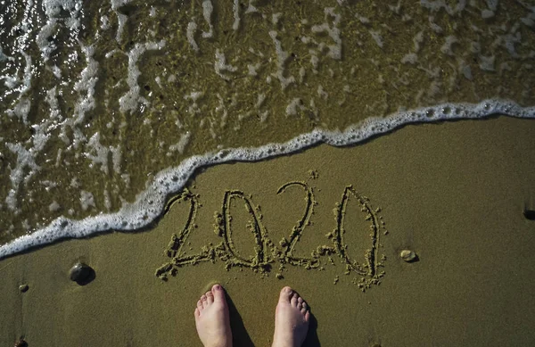 feet on the beach with Happy new year 2020 number written on sand. Top view. Happy new year concept, 2020 writing on sand beach