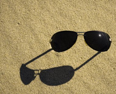 Güneşi ve gökyüzünü yansıtan plaj kumu üzerinde güneş gözlüğü. 