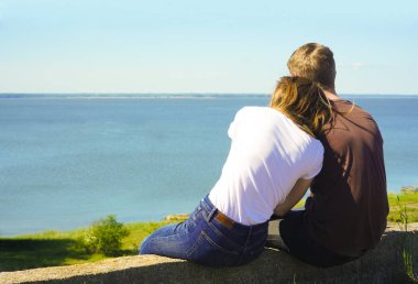 çatı veya brdge aşık genç çift. Geri, mavi bir gökyüzü ve deniz arka plan altında oturan bir erkek ve kadın çift arka görünümü. 