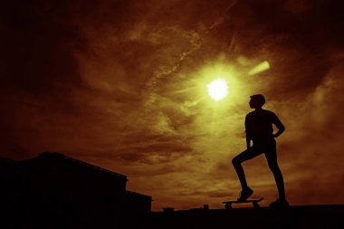 Kaykaycı iş başında. Güneş arka plan ile gökyüzünde paten parkta sörf paten hile yapan genç kadının siyah siluet. 