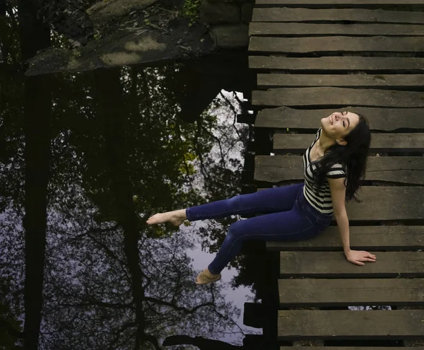 Νεαρή Γυναίκα Κάθεται Χαλαρή Ξύλινη Γέφυρα Πάνω Από Ποτάμι — Φωτογραφία Αρχείου