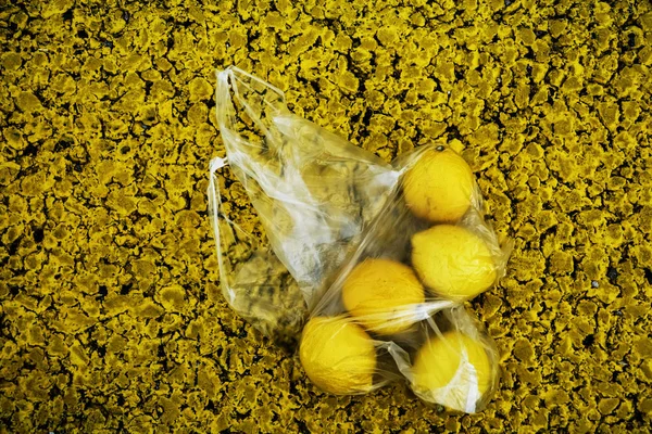 a lot of yellow lemons in a transparent packaging bag lie on asphalt road.