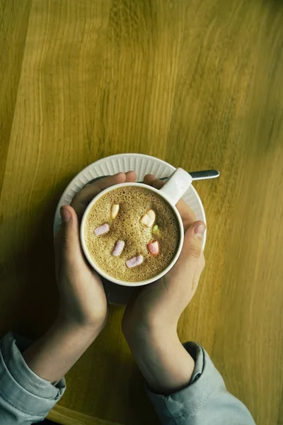 cup of cocoa with marshmallows in hands. Winter hot drink. girl warm hands from the mug with hot cocoa or chocolate with sweets on wooden table from above. top view.