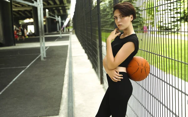 Sporty caucasian girl playing basketball - short haircut girl in a sporty wear. Portrait of a young woman holding a basketball ball