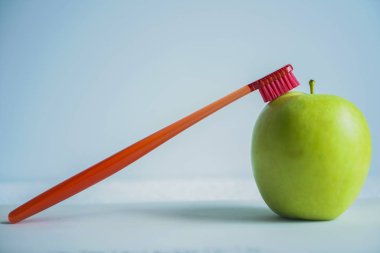 kırmızı diş fırçası ile yeşil elma, mavi arka plan üzerinde izole. sağlıklı diş bakımı kavramları