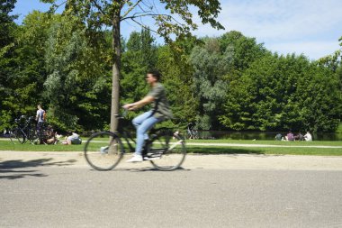 Sıcak bir yaz gününde Vondelpark. İnsanlar güneşin altında ağaçların altında çimenlerin üzerinde dinleniyorlar. Bisikletler yola çıkıyor. Amsterdam, North-Holland, Hollanda 