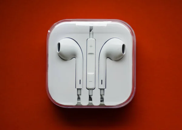 Modern earphones in plastic white  case with cable on red background, top view