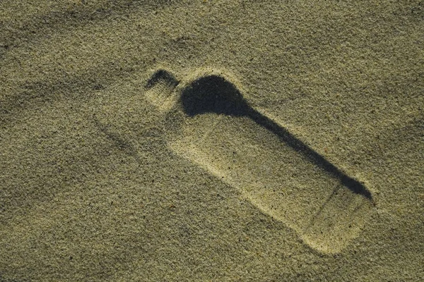 Empty bottle on the beach shore of an ocean,  symbol image for littering and ecological.