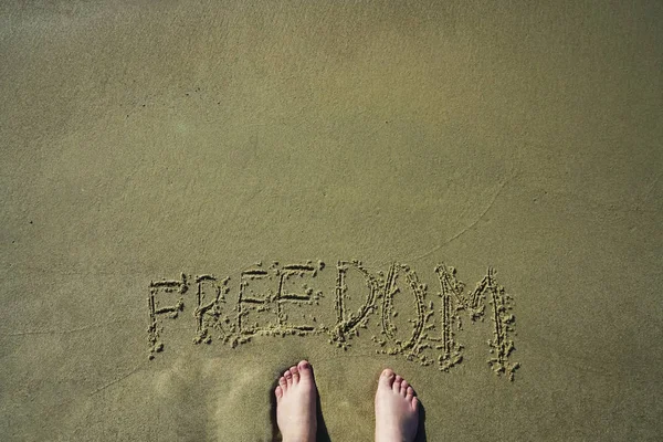 Concept or conceptual freedom text handwritten in sand on a beach with feet in an exotic island.free word written on the sand. Top view of human feet on summer beach