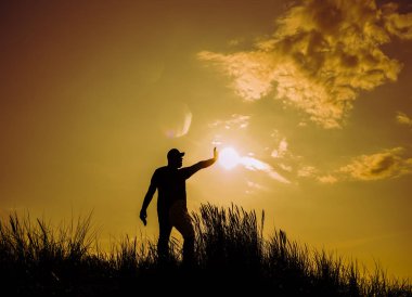 Gün batımında cep telefonu kullanan genç bir adamın silueti..  
