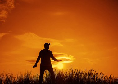 gün batımında cep telefonu kullanan genç bir adamın silueti. Tatil ve teknoloji konsepti.