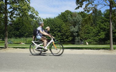 Vondelpark sıcak bir yaz gününde. İnsanlar güneşin altında ağaçların altında çimenlerin üzerinde dinleniyorlar. yolda iki Bisiklet sürme çift. Amsterdam, North-Holland, Hollanda 