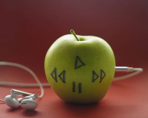 Zelené Jablko Kterém Jsou Připojeny Sluchátka Červené Pozadí — Stock fotografie