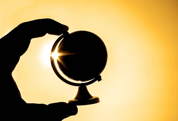 silhouette of Globe in male hand against sun and sunrise sky.