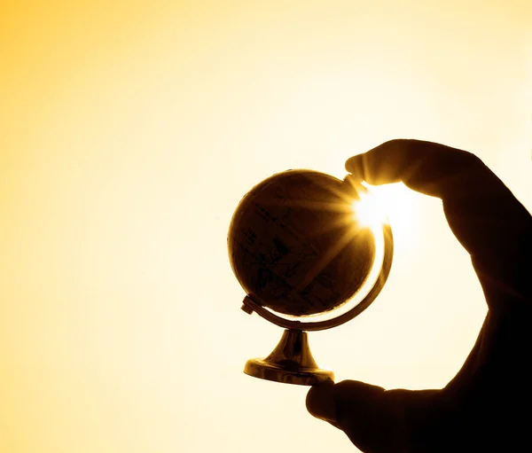 silhouette of Globe in male hand against sun and sunrise sky. Environmental protection concept.