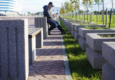 Ciddi bir genç adam cep telefonundan mesaj atıyor. Yakışıklı genç erkek bir bankta oturuyor ve akıllı telefonunu kullanıyor.. 