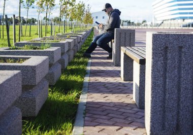 Ciddi bir genç adam cep telefonundan mesaj atıyor. Yakışıklı genç erkek bir bankta oturuyor ve akıllı telefonunu kullanıyor.. 