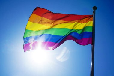 Gökkuşağı bayrağı (Lgbt hareketi) güneşli mavi gökyüzü arka planında 