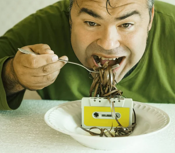 man eat Unspooled cassette tape on a plate with metal fork. Eating cassette on a dish for dinner