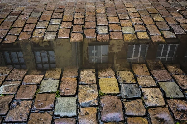 雨の中で水たまりに家の反射と石畳 水の上の円 舗装石 古いヨーロッパの通り — ストック写真