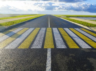 Beyaz ve sarı zebra yolda kesişiyor. siyah yeni modern asfalt. Bakış açısında boş ıslak yol. Yağmurdan sonra güneşli bir yaz günü