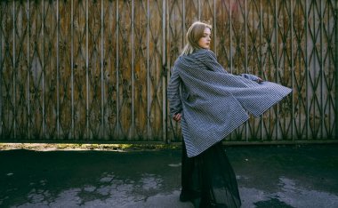 fashion and people concept - happy young woman or teenage girl spin with white and black plaid  coat on rusty iron fence background. 