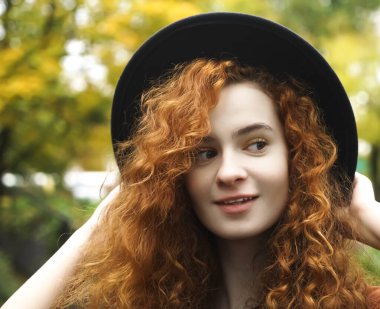 Ormanda siyah şapkalı hoş bir genç kız gün batımında arka planda ve uzaklara bakıyor. kızıl saçlı kıvırcık kadın siyah şapka takıyor.